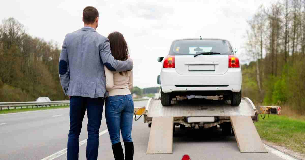 Couple watching as their car is loaded onto a flatbed tow truck during roadside assistance.